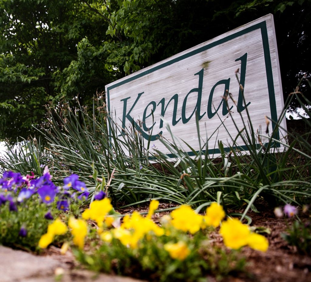 Kendal entrance sign with yellow and blue flowers in the foreground