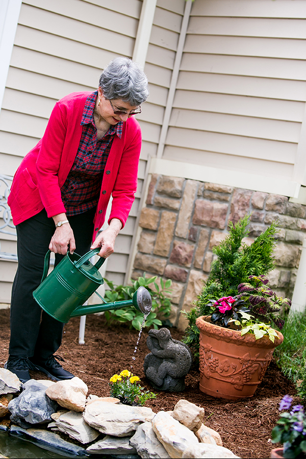 Female resident in red sweater watering flowers in her garden