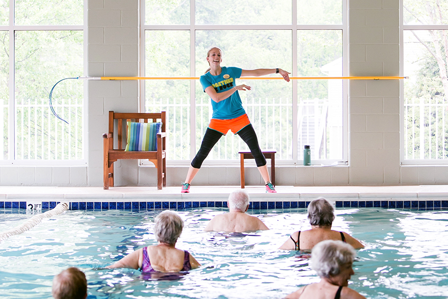 Female staff member leading aquatic therapy session for residents in a heated indoor pool